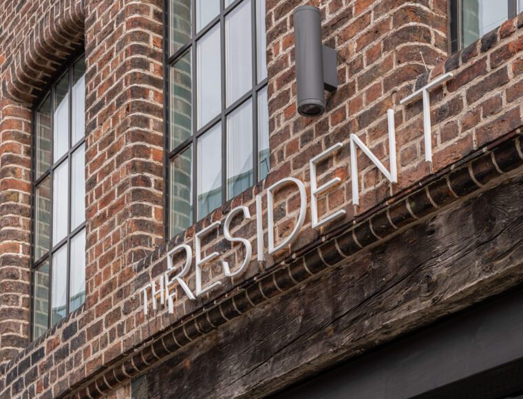 A close-up of a brick building's facade with large, rectangular windows. A modern sign reads 
