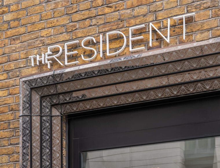 A brick wall with a black-framed entrance features illuminated white letters spelling 