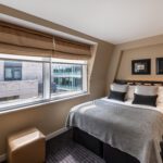 A small double room with a bedside table, double bed and stool.