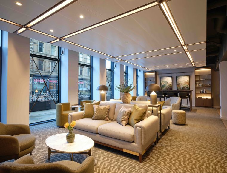 The Resident Edinburgh's modern lounge area with plush seating, a marble coffee table, and decorative plants. Large windows let in natural light, and stunning double fireplace.