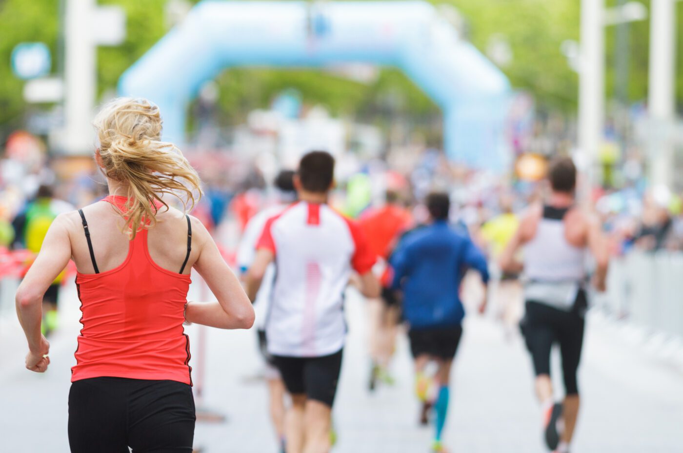 Runners competing in the TCS London Marathon along a city street, with a blurred background and an inflatable arch visible in the distance. The participants wear athletic gear, capturing the lively spirit of this outdoor event.
