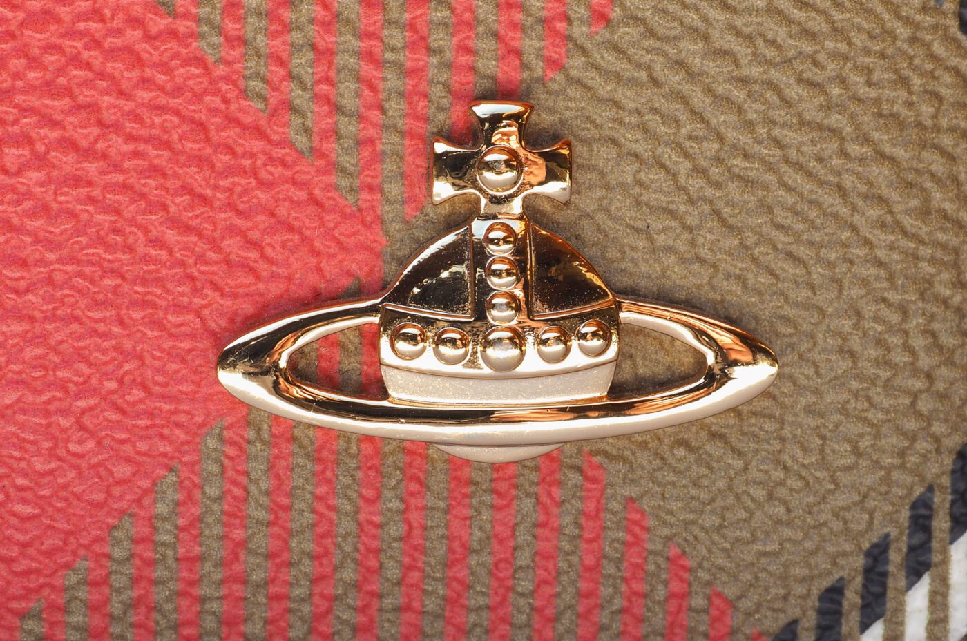 Close-up of a gold Vivienne Westwood orb logo on a wickedly textured, multicolored plaid background with vibrant red, green, and beige tones.